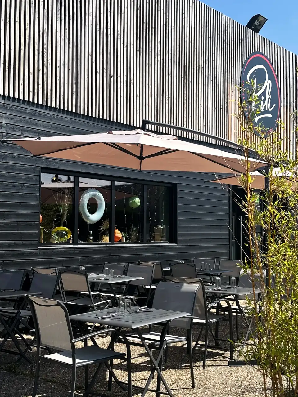 La devanture de Pili Pizza à La Frenaye : bardage en bois noir, enseigne ronde Pili sur le mur, terrasse dressée sous un parasol.