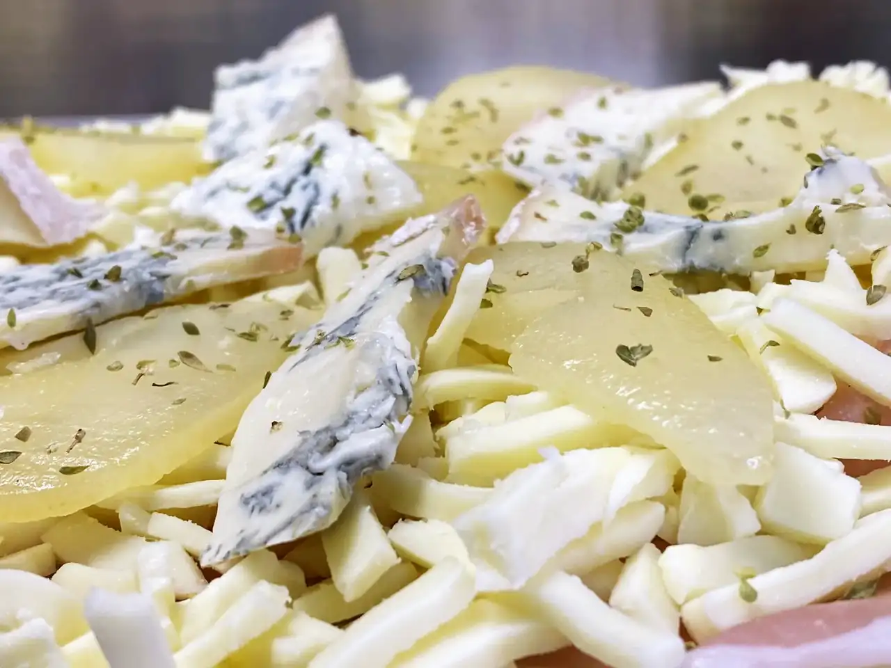 Avant cuisson : lamelles de pomme de terre, mozzarella râpée, morceaux de gorgonzola, jambon et origan.
